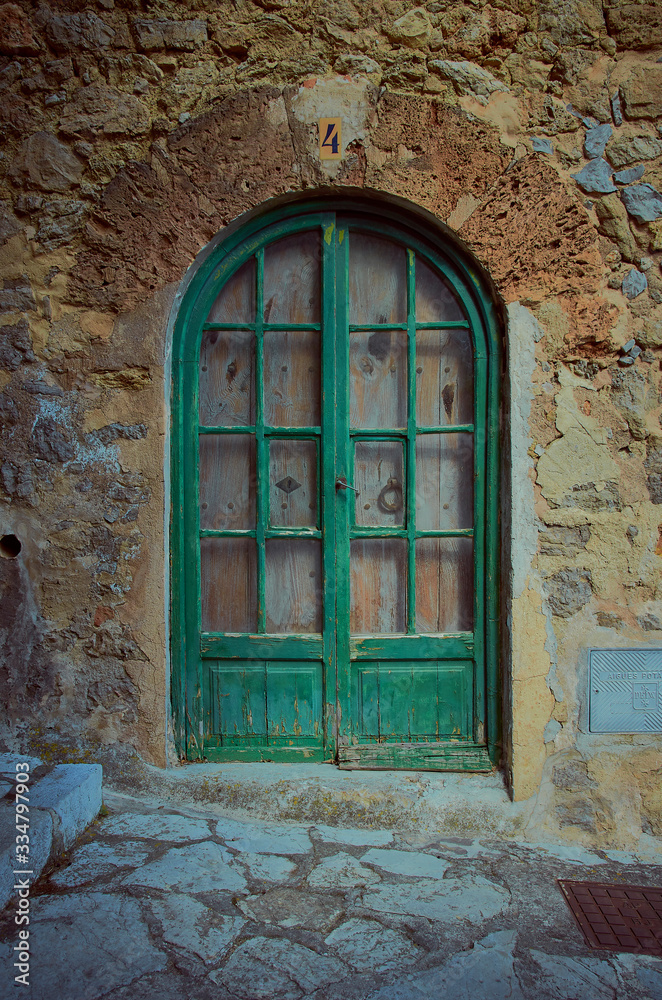 Wooden front door in a facade of an ancient house. The facade is made of stones and the street as well. It is summer in Mallorca, Spain.