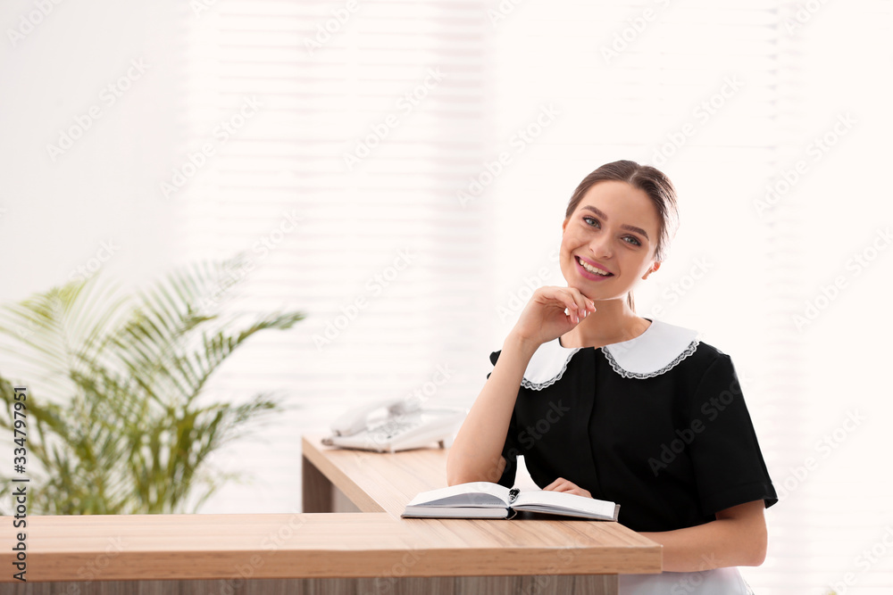 Young chambermaid near reception in hotel. Space for text