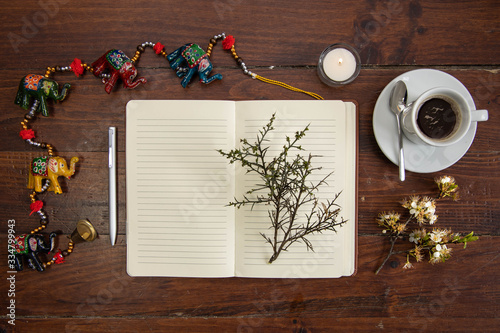 Composition with a notebook with a plant on top, a coffee, some elephant figures, and a candle on top of an old wooden table.