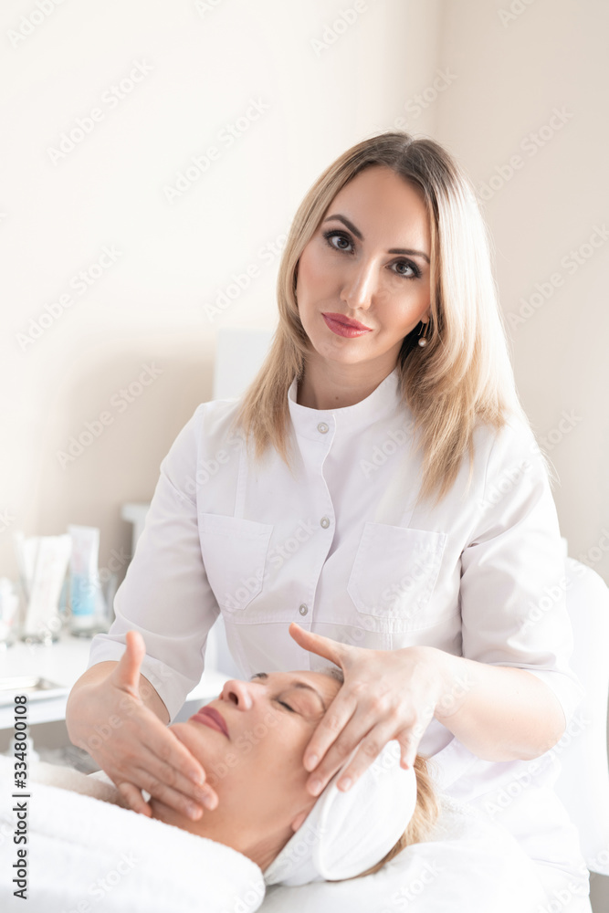 Portrait of attractive beauty professional in lab coat making facial massage to smooth out wrinkles of mature woman Portrait of attractive beauty professional in lab coat making facial massage to smooth out wrinkles of mature woman