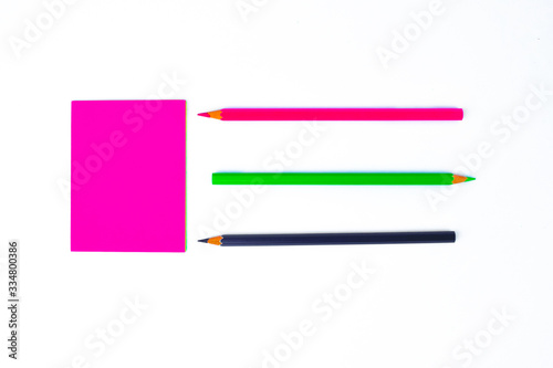 Top view of three different colored wood pencil crayons pointing at a pink sticky note
