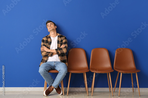 Waiting young man sitting on chair near color wall