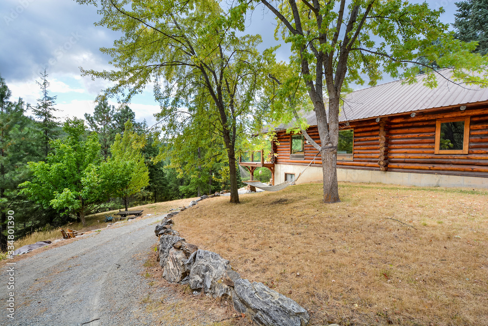 Fototapeta premium A rustic log cabin in a rural mountain setting with landscaped rocks and a hammock swing between two trees in the mountains of the USA.