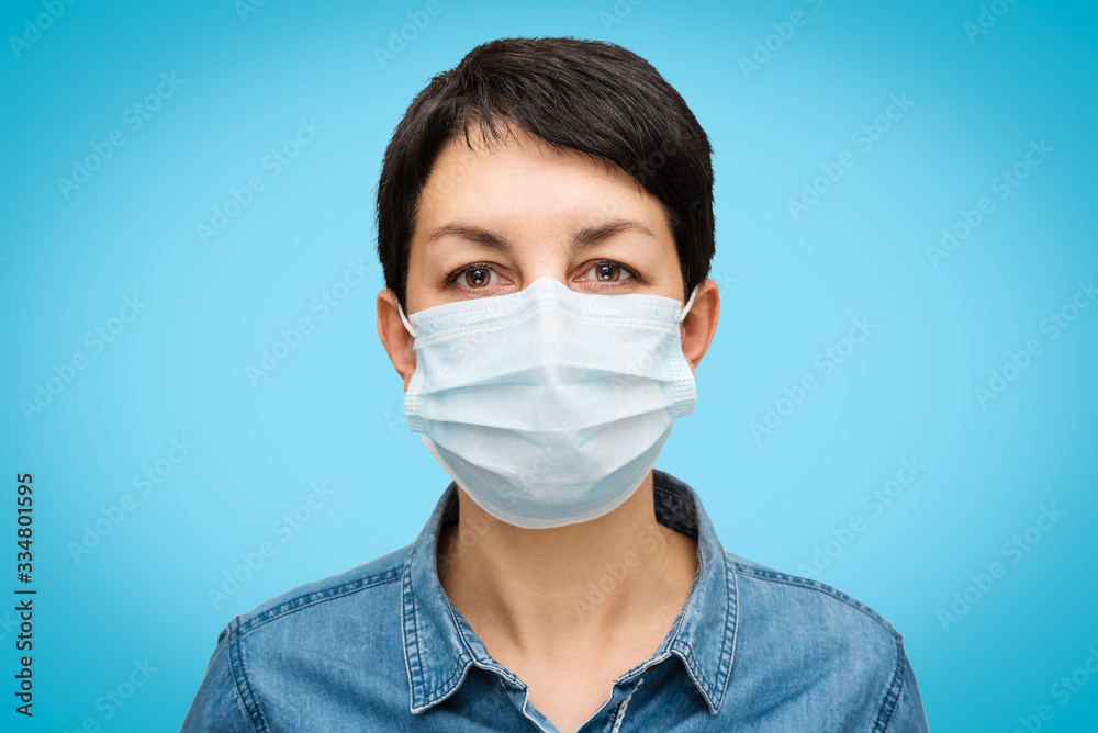 Studio portrait of young woman wearing face medical mask looking at camera on blue background. Close-up. Flu epidemic, dust allergy, protection against virus. Covid-19 outbreak, coronavirus pandemic Studio portrait of young woman wearing face medical mask looking at camera on blue background. Close-up. Flu epidemic, dust allergy, protection against virus. Covid-19 outbreak, coronavirus pandemic