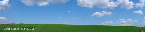 Panoramic photo of a green field hill and blue sky with a nice cloudscape.