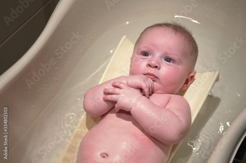 Infant baby boy washed in small bath tub, laying on back, view from above