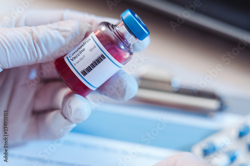 A bottle with a vaccine holds a specialist's hand in silicone gloves. Doctor fills the form after antiviral vaccine test. Vaccination in the form of tablets or injections. Hope for humanity. Epidemic.