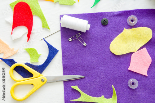 Colorful pieces of felt, scissors, needle, threads and pins on white wooden table. Table of seamstress. Craft concept 