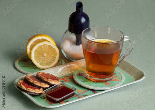 A cup of hot tea with lemon and sugar stands on a tray with jam and cookies with berry jelly and chocolate icing.