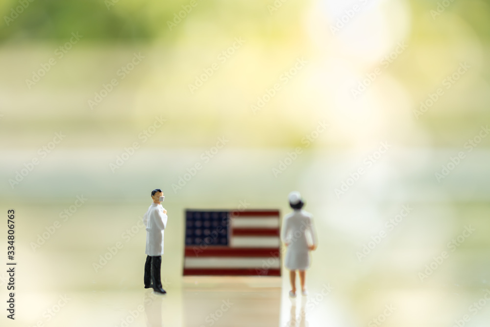 Global Healthcare, Coronavirus, Covid-19 Protection Concept. Doctor and nurse miniature figure people wearing face mask standing with United States of America (USA) flag pin with copy space. Global Healthcare, Coronavirus, Covid-19 Protection Concept. Doctor and nurse miniature figure people wearing face mask standing with United States of America (USA) flag pin with copy space.