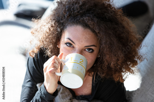 Young woman lies on couch and sipping from mug photo