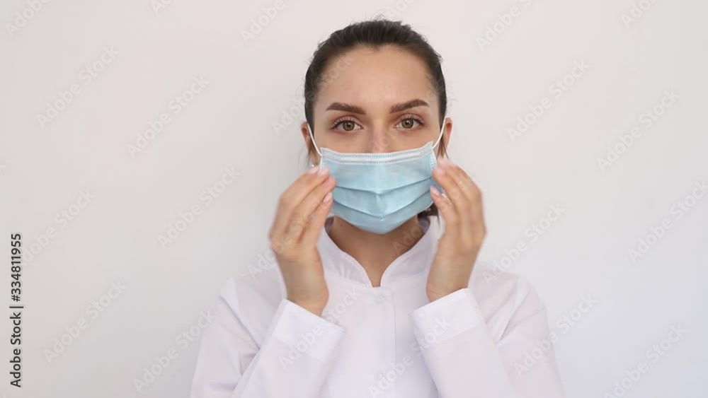 close-up young smiling doctor nurse woman girl in a white medical coat, puts on a medical protective mask, looks at the camera, hygiene concept covid-19, coronavirus, on a white background, close-up young smiling doctor nurse woman girl in a white medical coat, puts on a medical protective mask, looks at the camera, hygiene concept covid-19, coronavirus, on a white background,