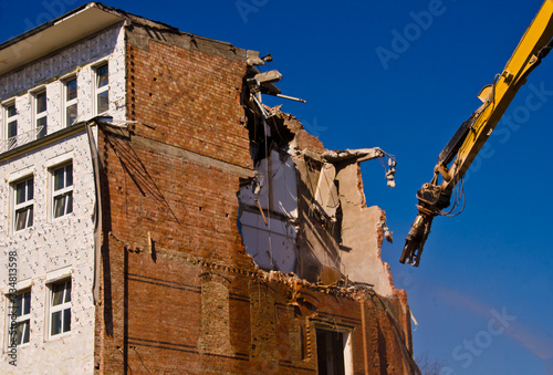 A demolition of a building with a crane with a blue sky background