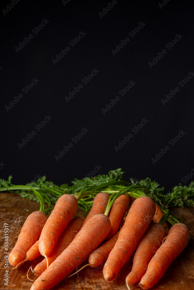 Top view of carrots, on weathered wooden table, with black background, vertical, with copy space