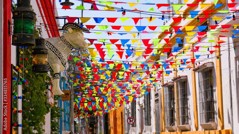 Beautiful and colorful colombian street with pennant flags decorating the houses, big statue in the shape of a cow wearing a typical Colombian hat. Colorful abundant fair flags on beautiful day.