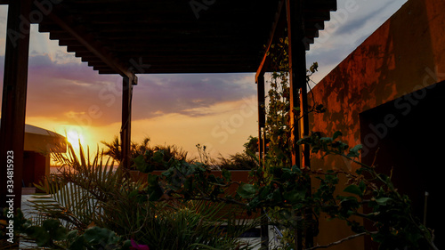 Beautiful sunset and warm colors on the rooftop of a house, with wood and plants, very peaceful looking house and sky.
