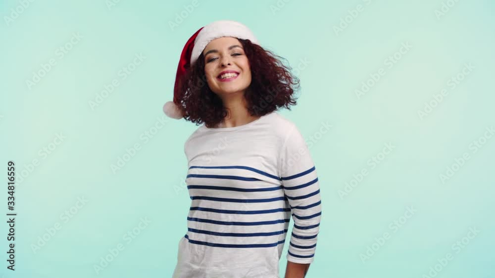 cheerful girl in santa hat waving hand and dancing isolated on turquoise cheerful girl in santa hat waving hand and dancing isolated on turquoise