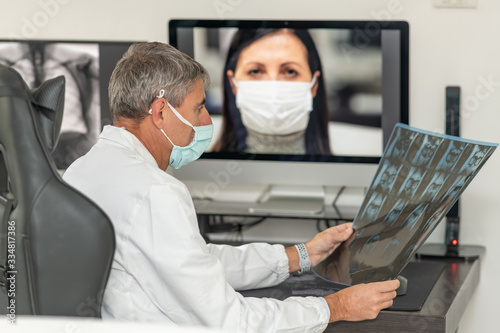 Back view of doctor making video call with his patient at home wearing mask. Close up of patient in video conferencing with general practitioner with computer. Sick girl in online consultation.