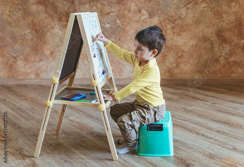 Young boy sits and drawing on drawing board with felt-tip pens