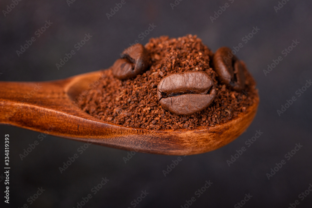 Ground and grain coffee in a wooden spoon against a dark background Ground and grain coffee in a wooden spoon against a dark background