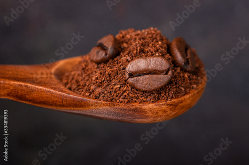 Ground and grain coffee in a wooden spoon against a dark background