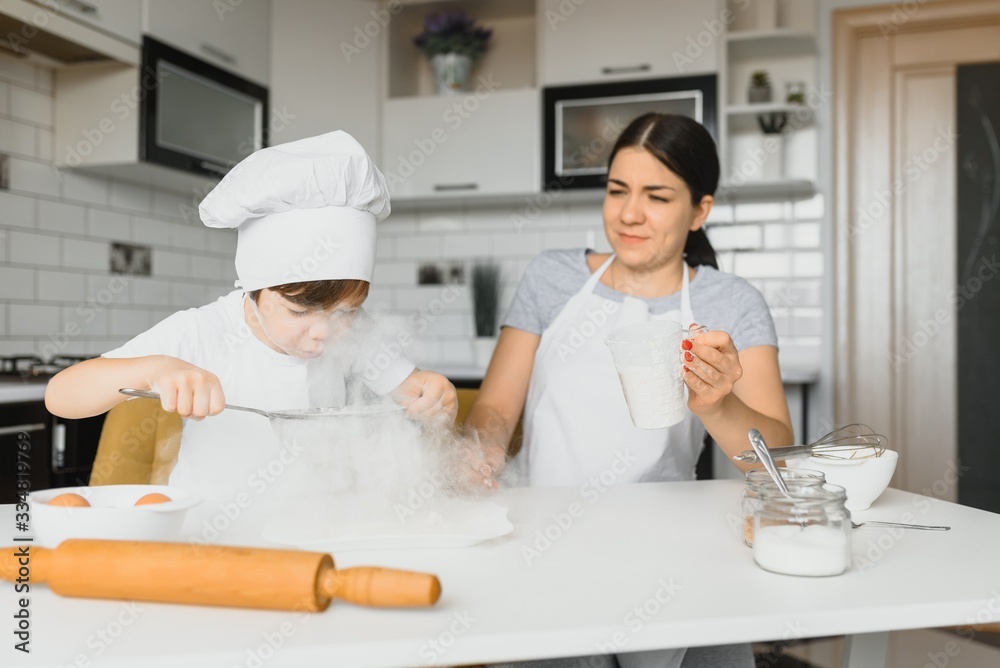 A young and beautiful mom is preparing food at home in the kitchen, along with her little son A young and beautiful mom is preparing food at home in the kitchen, along with her little son