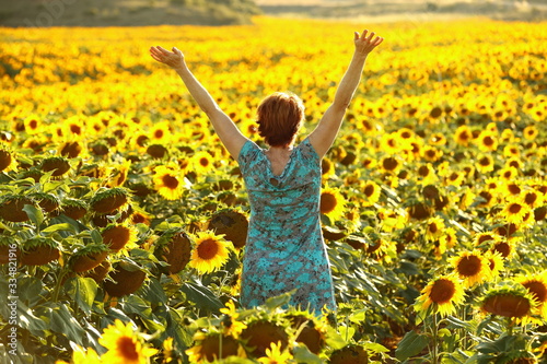 woman in blue dress happily walking through a yellow field ofsunflowers