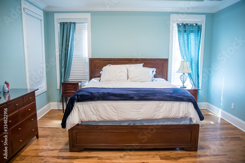 Large blue master bedroom with a king sized bed, furniture and drapes curtains on the windows with hardwood floors