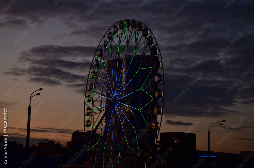 silhouette of a Ferris wheel against the sunset sky with clouds