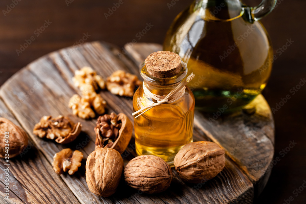 Concept of vegetable fat and oils for cooking and cosmetology. Glass bottle with bright yellow essence, raw walnut peeled and in their shells. Wooden board, dark wooden background, close up, macro Concept of vegetable fat and oils for cooking and cosmetology. Glass bottle with bright yellow essence, raw walnut peeled and in their shells. Wooden board, dark wooden background, close up, macro