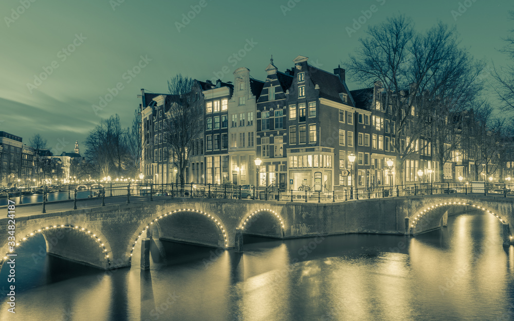 Amsterdam, the Netherland - March, 28th 2020 : Night scape of famous Amsterdam bridge with illuminated arcs long exposure shot at night with muted colors 
