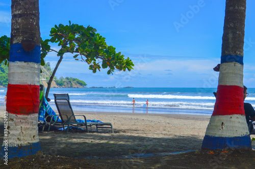 At Jaco beach, Costa Rica. With coloured painted palm trees with the flag of Costa Rica. A reclining chair under the shade of two palm trees and an 