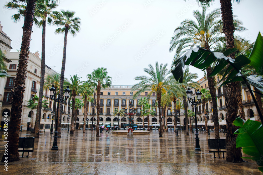 Placa Reial in winter with street restaurants at Barcelona, Catalonia. Rainy winter day, people with umbrellas