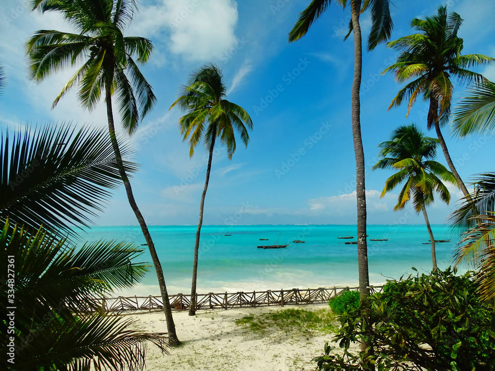 Traumkulisse Raffaello Werbung, Kokospalmen und Fernweh am weißen Strand mit türkisem Meer auf Sansibar, Fischerboote und Horizont im Hintergrund