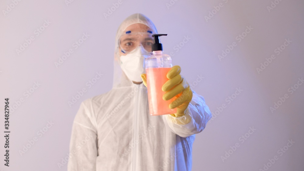 Man in a protective suit and protective medical mask holds in his hands dispenser and liquid soap.  Coronavirus or COVID-19 prevention.