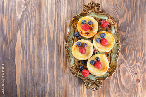 Small puff pastry tartlets stuffed with creme brulee and fresh blueberries and raspberries at a vintage tray on a wooden table, top view