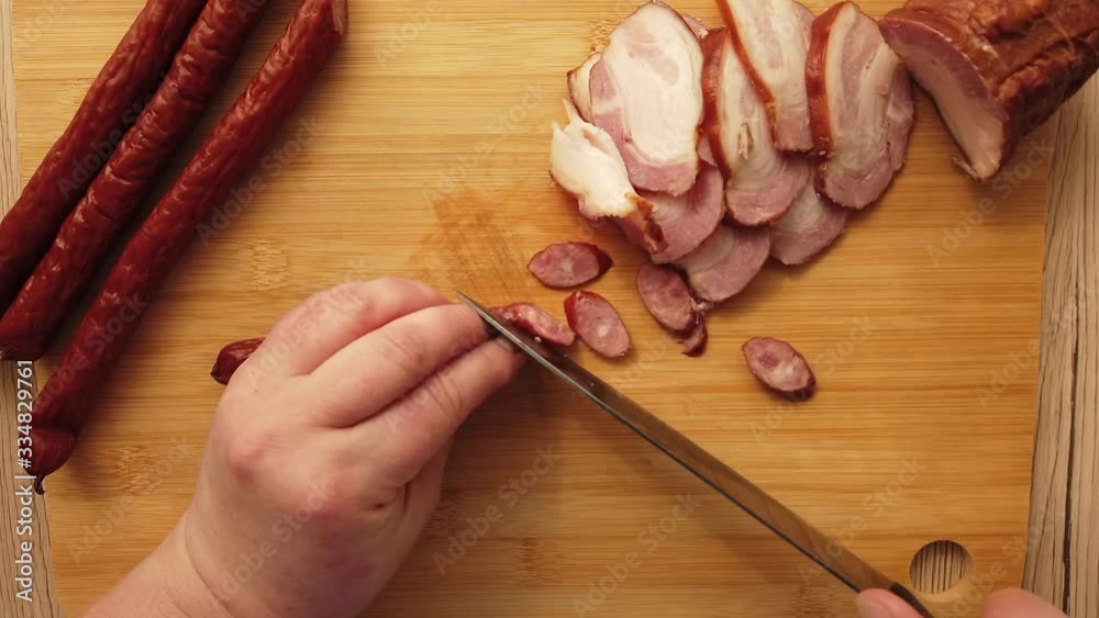 The cook cuts smoked sausage with bacon on a cutting board.