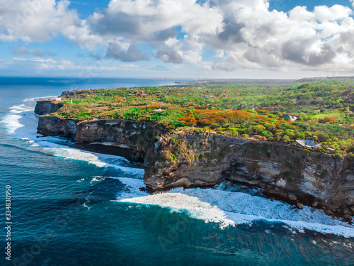 The sheer cliffs of the southern coast of Bali are washed by a clear azure ocean. Bukit Peninsula aerial view. Uluwatu temple on the rock.