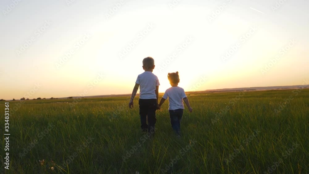 Children boy and girl walking on the green grass holding hands. Children boy and girl walking on the green grass holding hands.