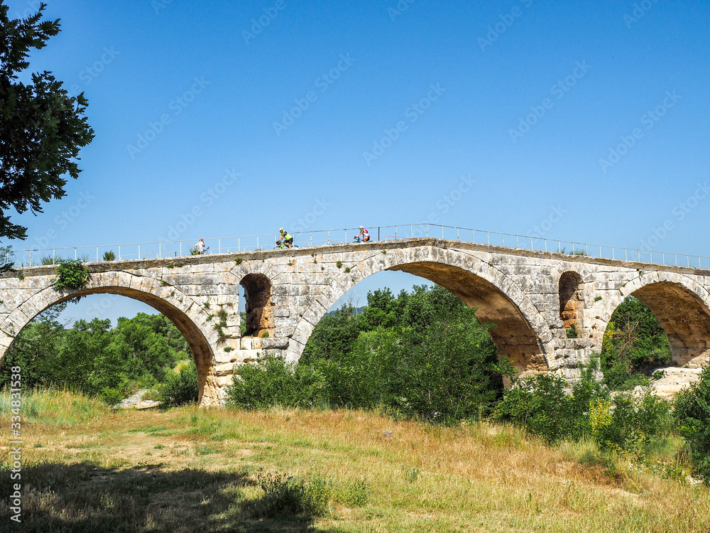 Bicyclists on an old stone bridge in the French countryside with blue sky and copy space.
