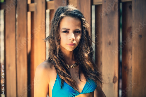 Portrait of a beautiful young girl in blue swimsuit leaned against a wooden fence.
