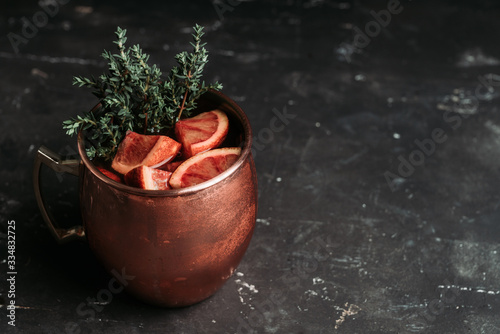 Red oranges cocktail in copper mug (variation of Moscow mule) on the wooden background. Selective focus. Shallow depth of field. photo