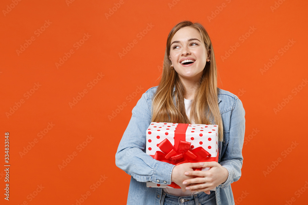 Funny pensive young woman girl in casual denim clothes isolated on orange background. Valentine's Day Women's Day birthday holiday concept. Hold red present box with gift ribbon bow, looking up aside. Funny pensive young woman girl in casual denim clothes isolated on orange background. Valentine's Day Women's Day birthday holiday concept. Hold red present box with gift ribbon bow, looking up aside.