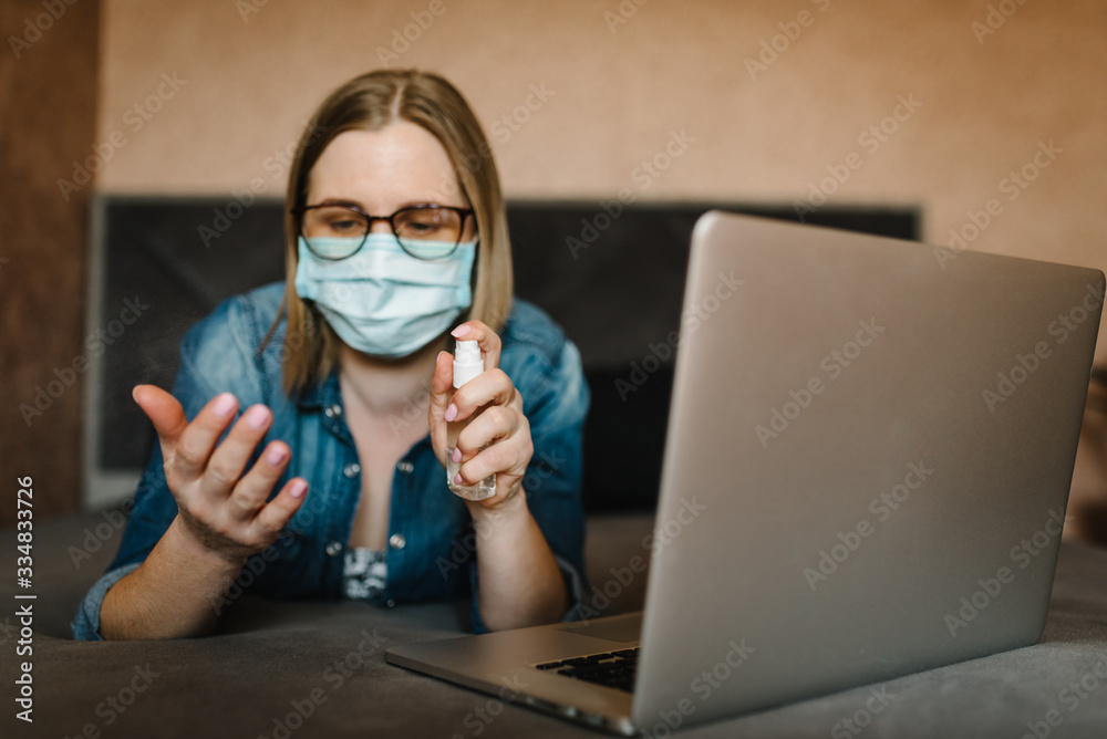 Coronavirus. Sanitizer.  Business woman working in home, wearing protective mask in quarantine. Cleaning hands antibacterial spray, sanitizer gel. Stay at home. Girl learns, using laptop. Freelance.