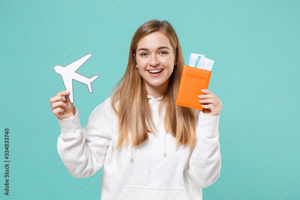 Smiling young woman girl in casual white hoodie posing isolated on blue turquoise wall background. People lifestyle concept. Mock up copy space. Hold passport tickets boarding pass paper air plane. Smiling young woman girl in casual white hoodie posing isolated on blue turquoise wall background. People lifestyle concept. Mock up copy space. Hold passport tickets boarding pass paper air plane.