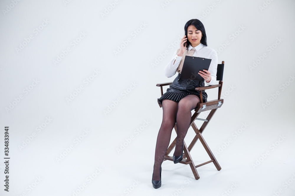 Successful business woman in a white shirt sitting on a chair with documents and talking about the business on the phone. Successful business woman in a white shirt sitting on a chair with documents and talking about the business on the phone.