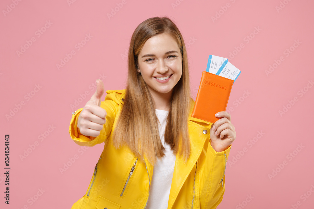 Smiling young woman girl in yellow leather jacket posing isolated on pastel pink wall background. People lifestyle concept. Mock up copy space. Hold passport tickets boarding pass, showing thumb up. Smiling young woman girl in yellow leather jacket posing isolated on pastel pink wall background. People lifestyle concept. Mock up copy space. Hold passport tickets boarding pass, showing thumb up.