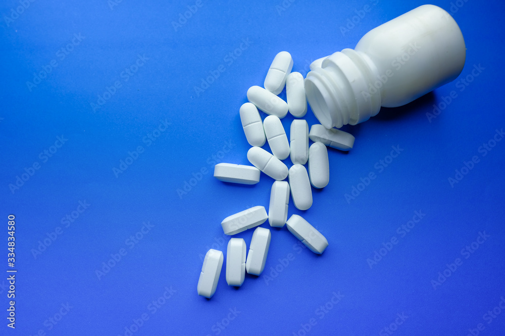color pills spilling from container on blue background, top view color pills spilling from container on blue background, top view