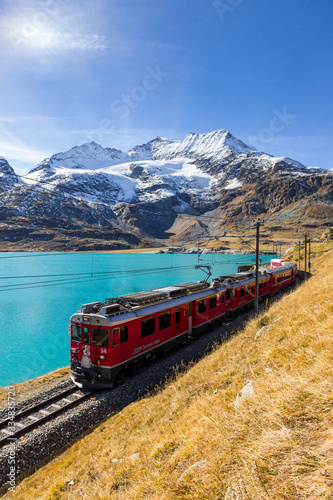Red train Bernina Express passing along Bianco lake in the Swiss alps, Graubunden, Switzerland