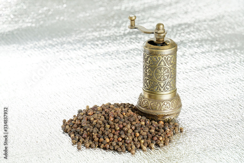 Black pepper and vintage mill on silver background. Spice grinder and heap of grains of pepper. Sample for packing